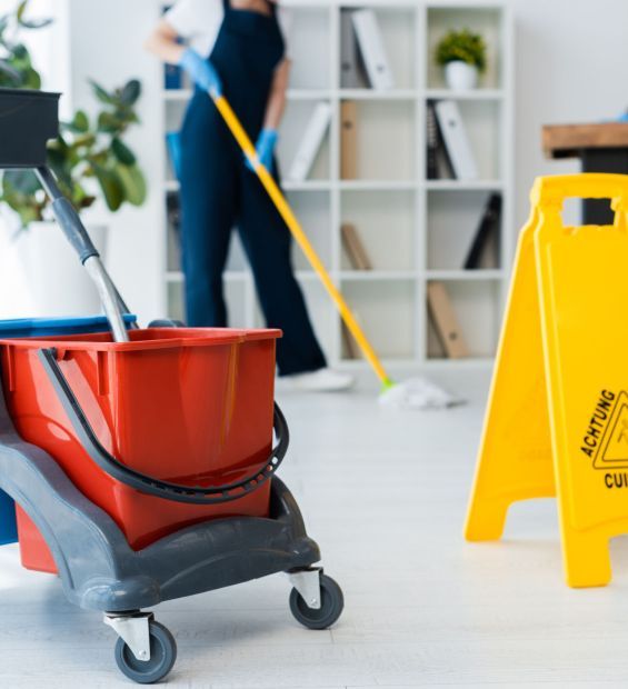 Selective focus of cleaning trolley near wet floor sign and multiethnic cleaners working in office