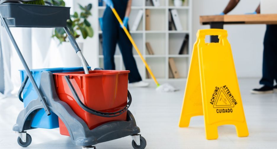 Selective focus of cleaning trolley near wet floor sign and multiethnic cleaners working in office